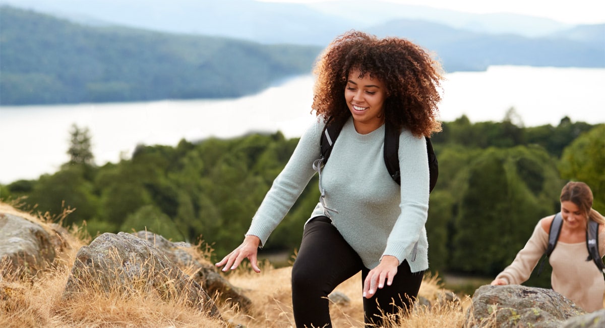 two friends practicing social distancing while smiling and hiking up a mountain