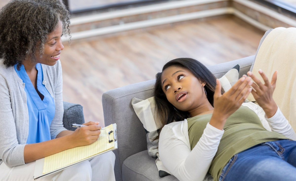 Black female mental health professional listening to patient as she lays on the couch and talks freely