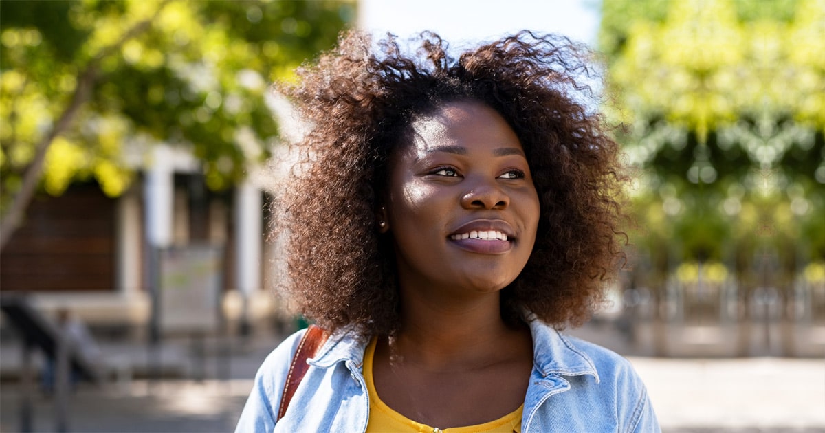 natural haired black woman smiling while looking away onto the street and thinking