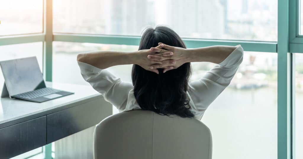 business woman reflecting at her desk with hands folded behind her head